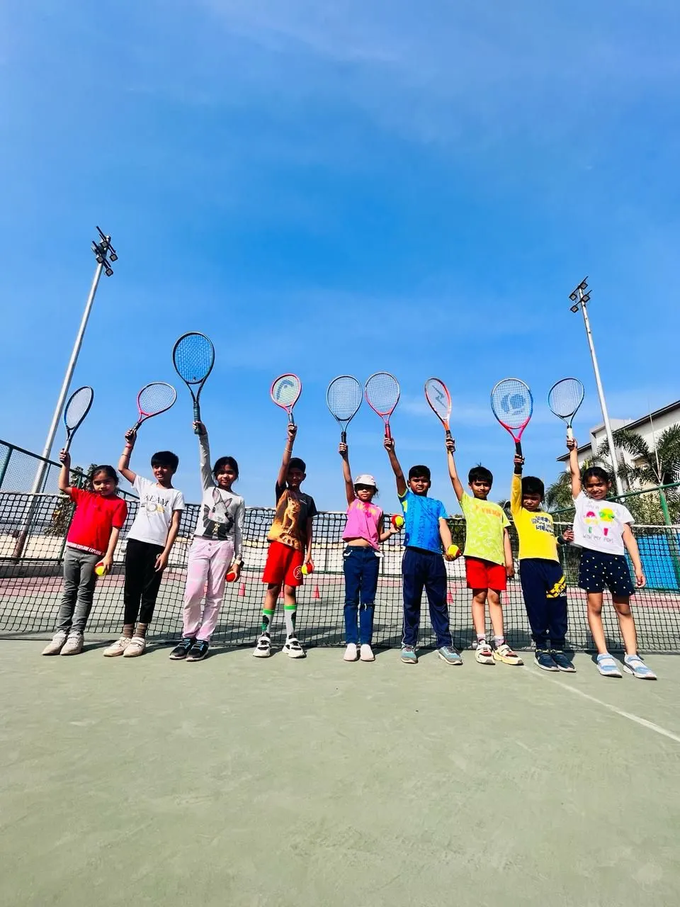 Young PLAY n FIT players raising their racquets in a line in front of the net